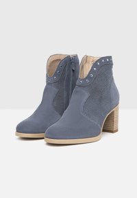 Bottines bleues avec une finition en suedine et des panneaux en maille, dotées d'une fermeture éclair sur le côté, d'un bout rond et d'un talon en bois empilé. Des clous argentés accentuent le dessus.