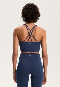 Tengerészkék sportmelltartó, hátul keresztpántos kialakítással, sima anyagból; magas derekú leggings-szel párosítva.