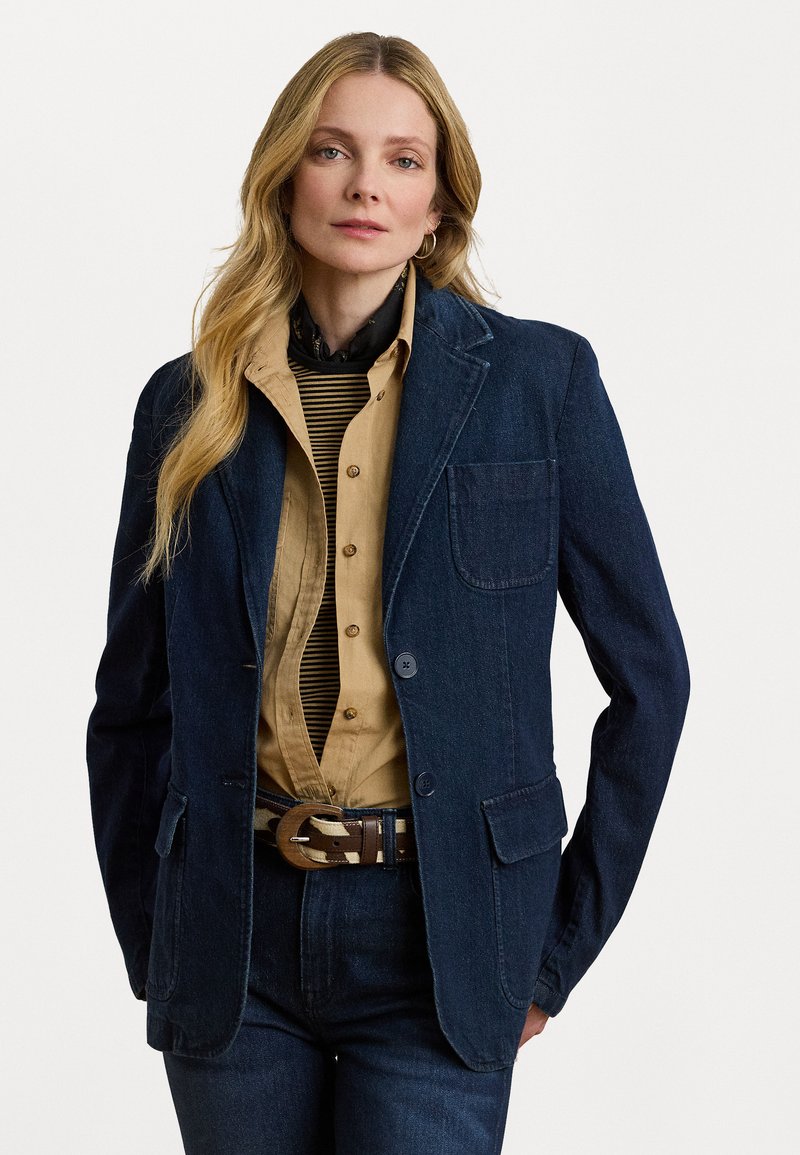 Donkerblauwe denim blazer met notch-kraag, twee voorzakken, knoopsluiting en een gestructureerd inner shirt. Een bruine met patroon riem maakt de look compleet.