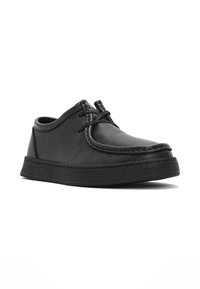 Chaussure décontractée en cuir noir avec un design moc toe, fermeture à lacets et semelle en caoutchouc texturée, montrée en angle trois quarts.