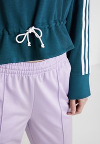 Teal, kort sweatshirt med vit dragsko, parat med lavendelfärgade joggers med elastisk midja. Har vita sportstripes på ärmarna.