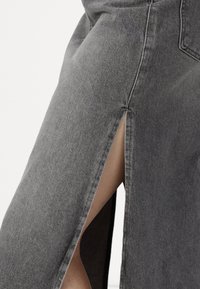 Grauer Denim-Rock mit einem seitlichen Schlitz, der aus einem strukturierten Stoff mit sichtbaren Nähten gefertigt ist. Das Design hat einen geraden Schnitt und klare Linien.