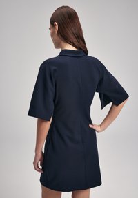 Laivaston sininen lyhythihainen mekko, jossa on kaulus, suora leikkaus, sivutaskut ja sileä pinta, näkyy takaa.