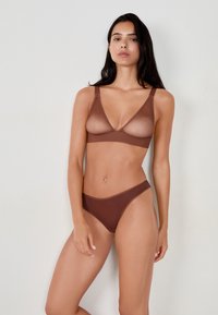 Brązowy zestaw bielizny zawierający przezroczysty top z regulowanymi ramiączkami oraz dopasowane majtki typu bikini o niskim stanie, wykonany z gładkiego materiału.