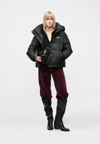 Black puffer jacket with a hood, quilted design, worn over a black top; paired with burgundy corduroy pants and black knee-high boots.