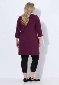 Bordeauxfarvet tunika med trekvartærmer, parret med sorte leggings og flade sorte sko; glat stof og afslappet pasform.