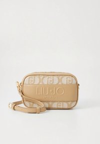 Beige crossbody bag with textured fabric and smooth leather accents. Features engraved logo and detachable strap. Zipper closure on top.