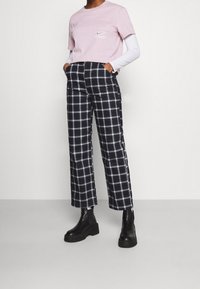 Ljusrosa t-shirt med korta ärmar och liten ficka, tillsammans med svarta och vita rutig cropped-byxor och svarta platåstövlar.