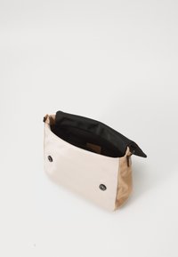 Borsa a spalla con texture satinata in crema e marrone, dotata di un interno nero, bottoni a scatto frontali e una tasca con zip per una chiusura sicura.