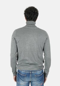 Maglione a collo alto grigio in morbido maglione, design aderente, maniche lunghe, collo a coste, indossato con jeans denim blu strappati.