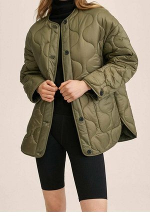 Veste matelassée vert olive avec col rond, boutons-pression et coupe volumineuse, associée à un short de cyclisme noir. Texture lisse.