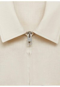 Krämfärgad skjorta med krage, synlig dragkedja och stickade detaljer; tillverkad av textil med struktur, som visar en ren, minimalistisk design.