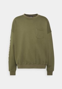 Olivgrön sweatshirt gjord av en bomullsblandning, med rund halsringning, långa ärmar, en bröstficka och tryckt text på ärmen.