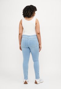Light blue skinny jeans with a high waist, five-pocket design, and visible stitching details, paired with a white tank top and athletic shoes.
