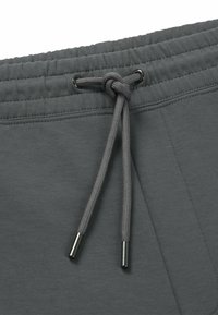 Grijze sportshorts hebben een elastische tailleband met een trekkoord en metalen uiteinden. Glad materiaal met zijnaaddetails.
