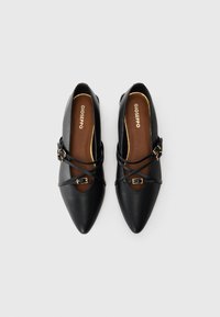 Ballerine in pelle nera con punta appuntita, dotate di cinturini incrociati neri e una fibbia in tonalità oro. Soletta marrone con il nome del marchio impresso.