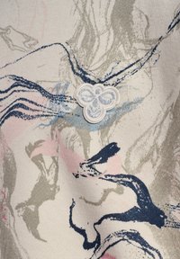 Bawełniana tkanina z abstrakcyjnymi falami w kolorach niebieskim, różowym i szarym, z wyraźnym białym haftowanym emblematem motyla.