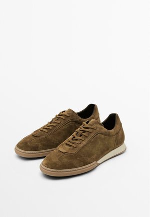 Braune Wildleder-Sneaker mit niedrigem Schnitt, geschwungenen Akzenten und beigen Gummisohlen. Ausgestattet mit flachen Schnürsenkeln und minimalistischen Nähten.