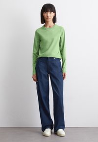 Groene lange mouwtop gecombineerd met donkerblauwe wijde jeans. Witte sneakers maken de outfit compleet, met een eenvoudig ontwerp en gladde texturen.
