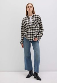 Camicia a quadri nei colori nero e crema, con tasca frontale; abbinata a jeans blu chiaro a gamba larga e stivaletti neri.