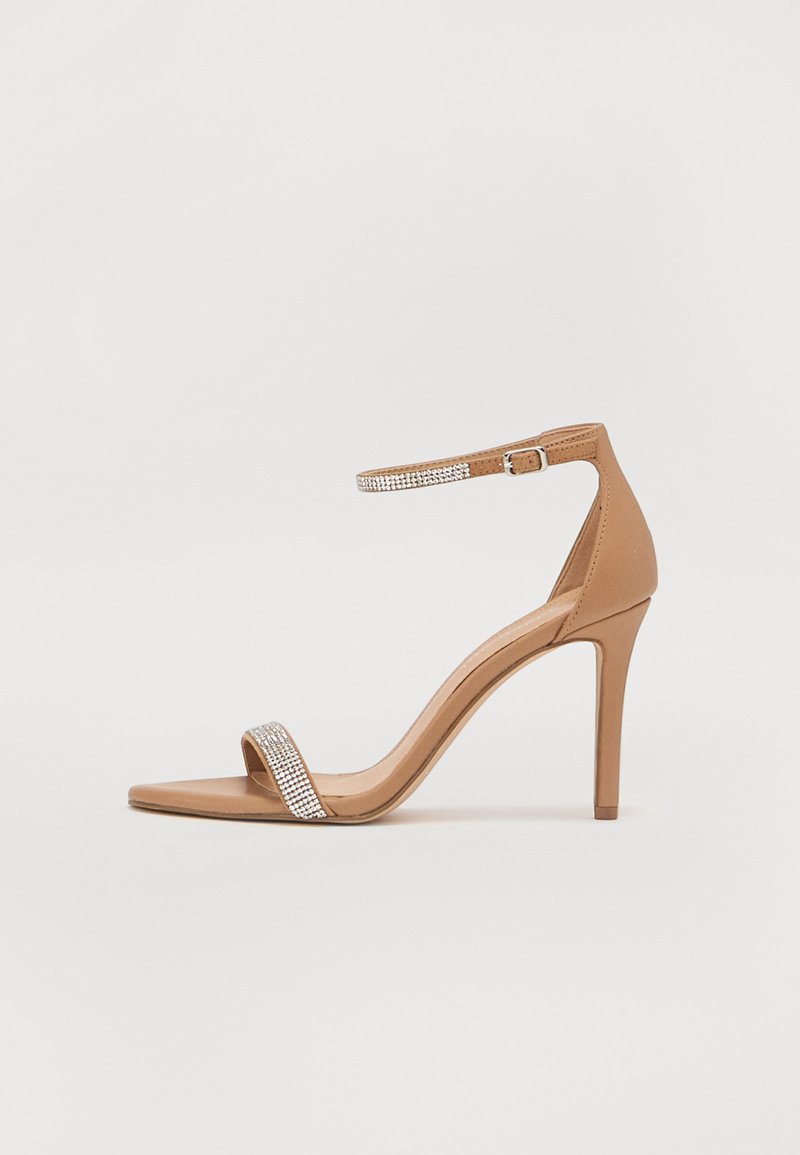 Tan high-heel sandal with a pointed toe, featuring a crystal-embellished strap and a thin ankle strap. Smooth texture and sleek design.