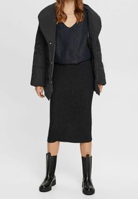 Cappotto piumino nero sopra un top scuro e lucido e una gonna midi nera aderente e scintillante. Completato con stivaletti neri lisci alla caviglia.