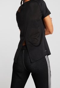 Top deportivo negro con paneles de malla, mangas cortas y una abertura en la parte trasera. Combinado con pantalones negros texturizados con franjas blancas.