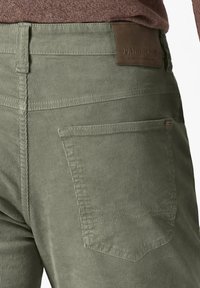 Olive green corduroy pants with a textured surface, featuring a leather logo patch at the waist and a single back pocket.