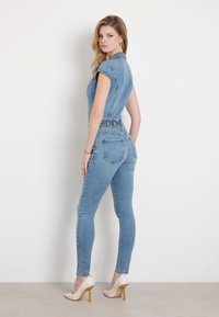 Traperice na kombinezon u svijetloplavoj boji s prilagođenim dizajnom, kap sleeves i pojasom u struku. Upareno s nude cipelama na visoku petu.