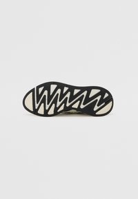 Semelle de sneaker noir et blanc avec un motif en zigzag, des zones de grip texturées et une semelle extérieure crème contrastante.