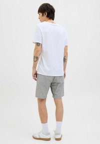 White crew-neck t-shirt with short sleeves paired with gray shorts, white socks, and sneakers featuring gray accents and a beige outsole.