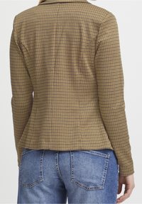 Veste à carreaux marron et jaune avec une coupe ajustée. Dotée d'un col à revers et de manches longues. Associée à un jean bleu délavé.