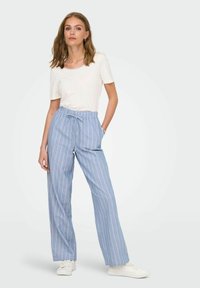 Helehallid triibulised laia lõikega püksid, mille värvel on elastne ja käepärased taskud, kombineeritud liibuva valge t-särgi ja valgete tossudega.