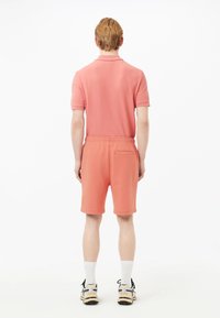 Polo de color coral y pantalones cortos a juego, hechos de una tela suave. Los pantalones cortos tienen una cinturilla elástica y un bolsillo trasero. Calcetines blancos y zapatillas deportivas.