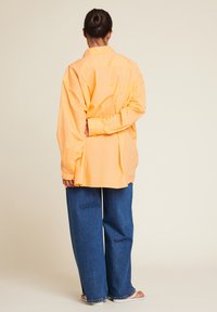 Langermet, skjorte med krage i lys orange, laget av bomull. Sammen med vide, blå denimjeans og enkle sandaler.