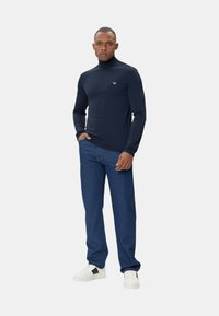 Maglia a collo alto di colore blu navy in tessuto liscio, abbinata a jeans di denim blu e sneakers bianche con dettagli neri.