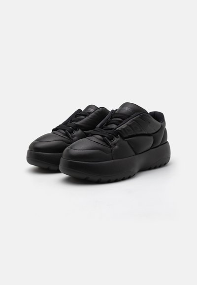 Baskets noires de sport avec une tige en cuir lisse, bout rond, semelle texturée, col rembourré et fermeture à lacets. Design minimal sans motifs.