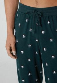 Teal katoenen broek met een elastische tailleband en verstelbaar trekkoord, met een herhaald patroon van zwart-witte biljartballen met het nummer acht.