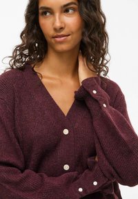 Cardigan lavorato a maglia in borgogna con scollatura a V, caratterizzato da una texture a coste, grandi bottoni e maniche lunghe con polsini abbottonati.