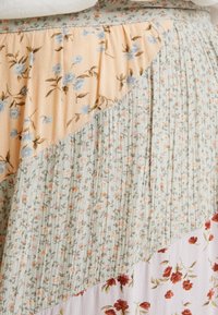 Jupe florale avec design à couches : tissus pêche clair, vert et lavande, présentant des motifs floraux variés et une texture plissée douce.