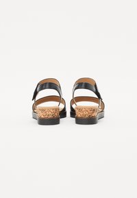 Black leather sandals with cork heel, adjustable ankle strap, open back design, flat sole, textured cork detailing, and brown insole.