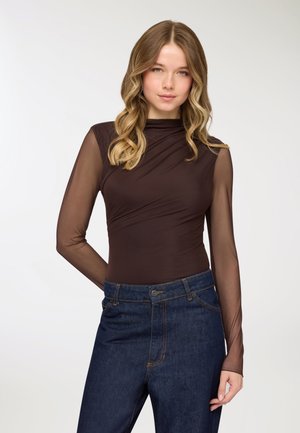 Top aderente marrone con maniche lunghe trasparenti, scollo tondo e design drappeggiato, abbinato a jeans blu scuro a vita alta.