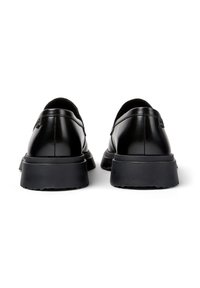 Un par de mocasines de plataforma de cuero negro mostrados desde atrás, con suelas de goma anchas, sobre un fondo blanco.