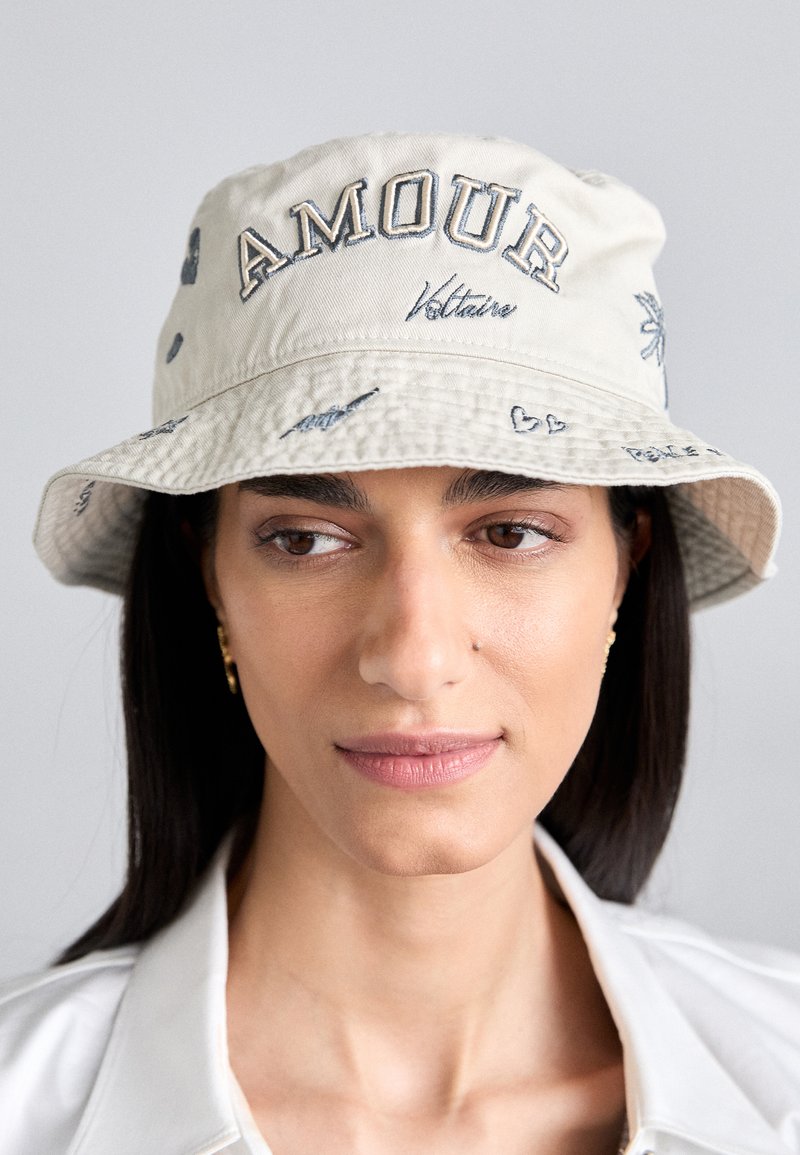 Bežna kapa s küralom, izrađena od pamuka, s izveznim tekstom "AMOUR" i "Voltaire", uz motive srca i teksturiranu obrub.