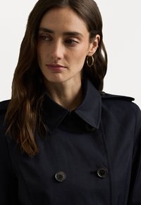 Marine trenchcoat met een dubbelzijdig ontwerp, grote kraag en zwarte knopen; heeft een gladde stofstructuur.
