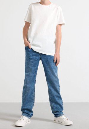 White short-sleeve t-shirt paired with blue jeans. The jeans are straight-leg style with a faded wash, complemented by white sneakers.