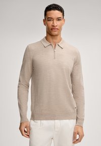 Beige Langarm-Polo-Pullover mit Reißverschlusskragen und geripptem Saum. Stricktextur, flach gestricktes Design, kombiniert mit weißen Hosen.
