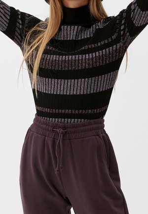 Maglione a righe nere a coste con accenti viola brillanti, colletto alto, abbinato a pantaloni della tuta viola con cordini. Tessuto morbido, vestibilità rilassata.