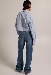 Light blue cropped shirt made of smooth fabric, paired with high-waisted, loose-fitting dark denim jeans with back pockets and stitching details.