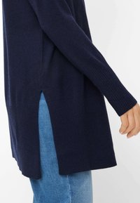 Maglione navy a maglia con polsini a coste e aperture laterali. Texture morbida e design allungato abbinato a jeans denim azzurri.